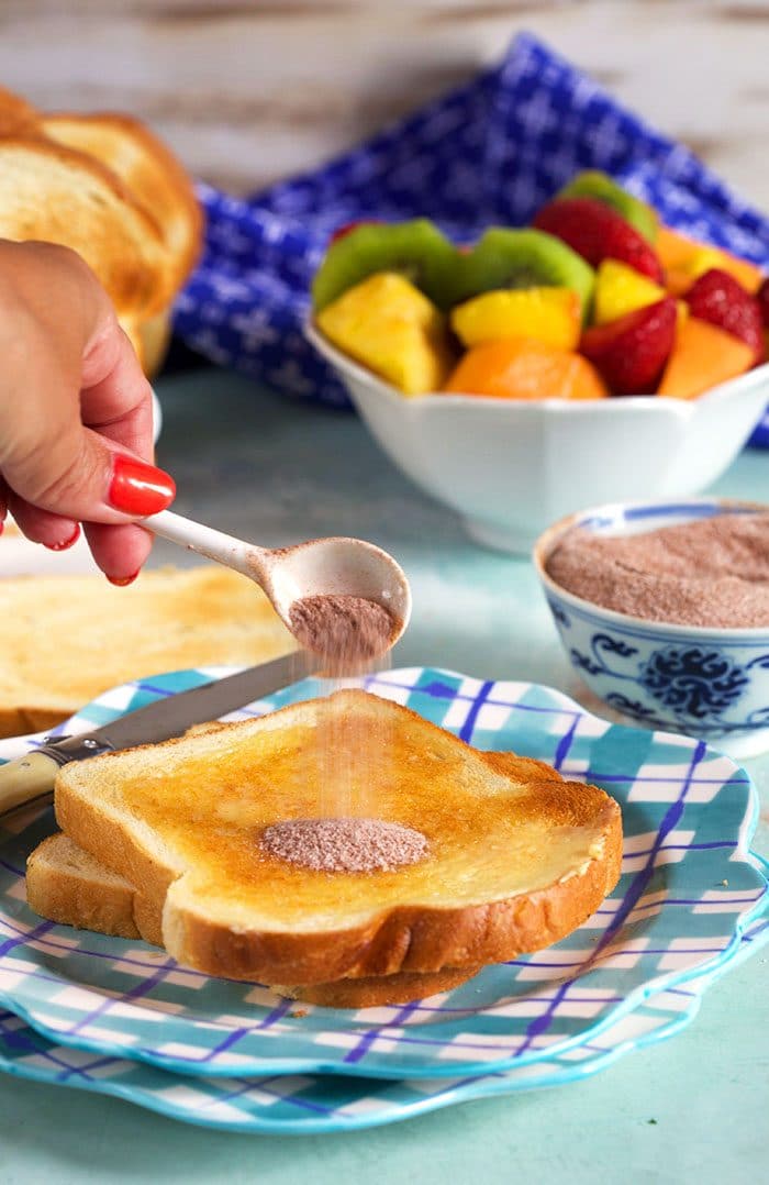 cinnamon sugar being sprinkled on a piece of cinnamon toast with a white spoon.