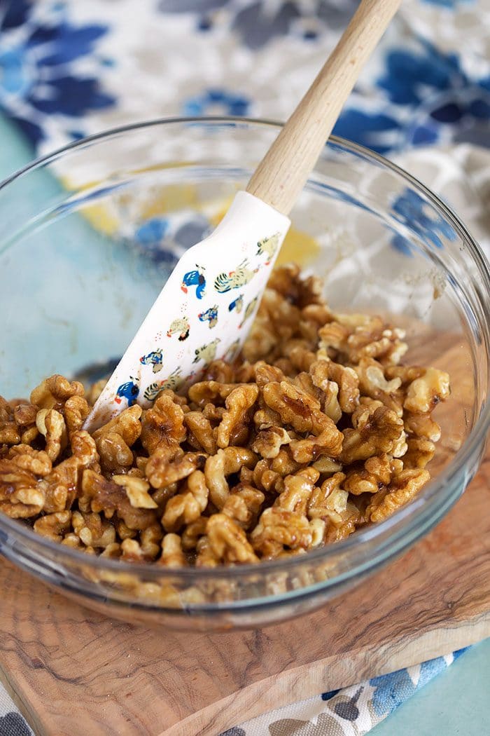 Walnuts being stirred in a glass bowl with a white spatula.