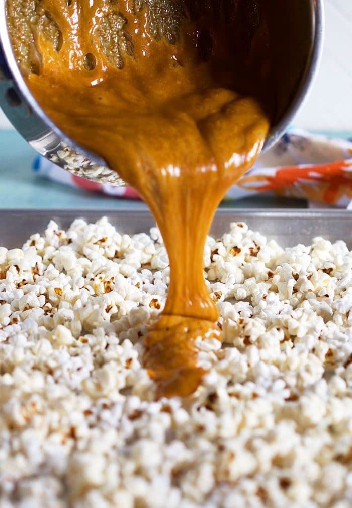 Caramel sauce being poured over popcorn on a baking sheet.