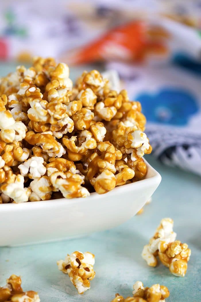Close up of caramel corn in a white bowl on a blue background.