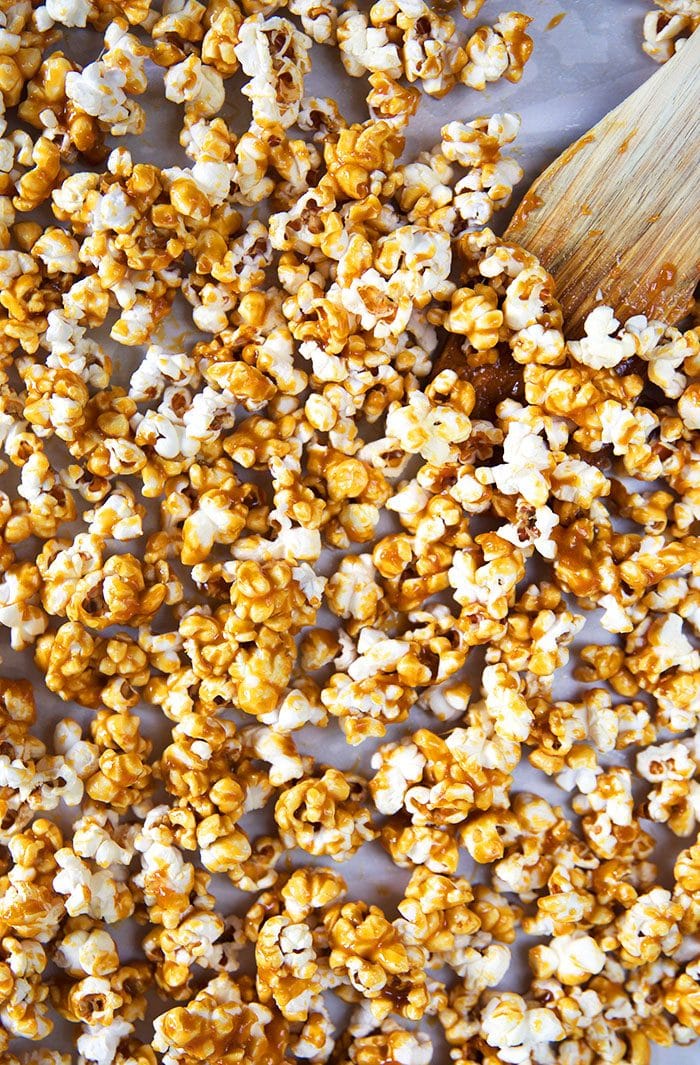 Overhead shot of caramel corn on a baking sheet with a wooden spoon.