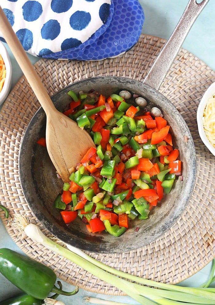 sauteed peppers and onions in a skillet with a blue and white polka dot mitt.