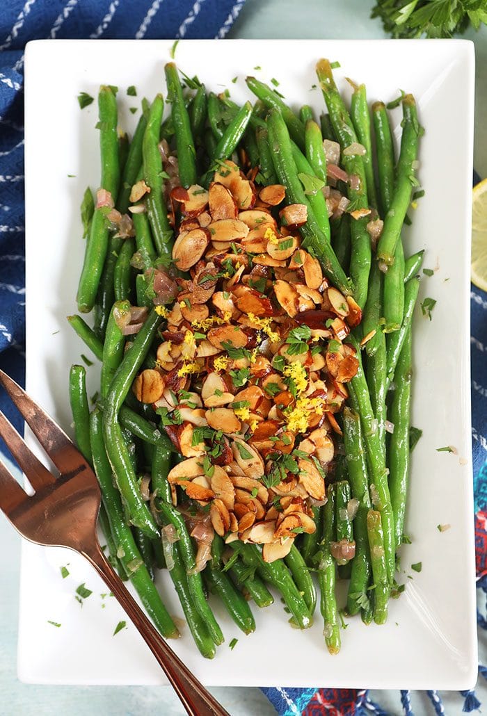 overhead shot of green beans almondine on a white rectangular platter.