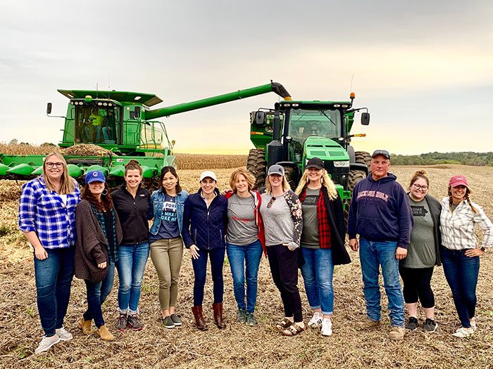a line of people in a corn field standing in front of a combine.