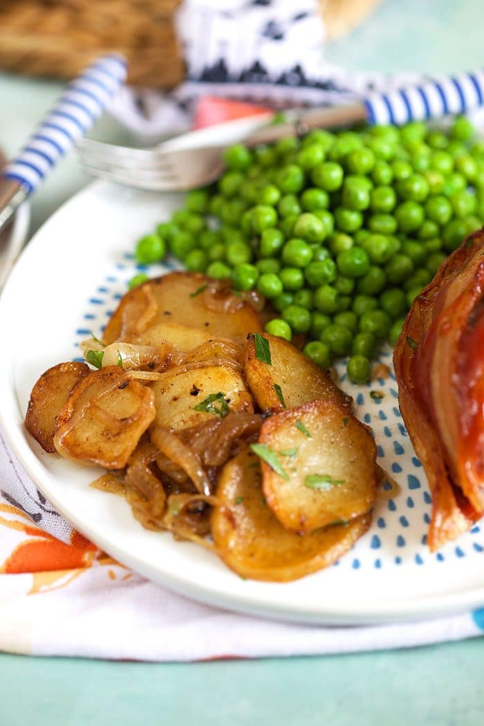 Lyonnaise potatoes on a white plate with peas and meatloaf. 