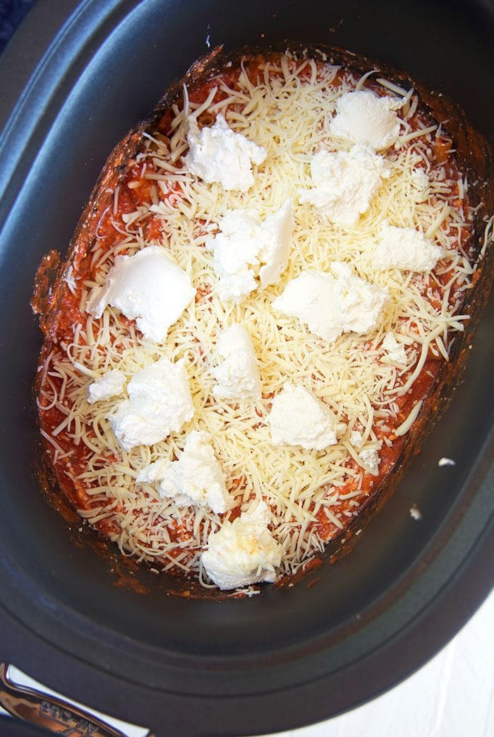 cheese sprinkled on top of pasta in a slow cooker.