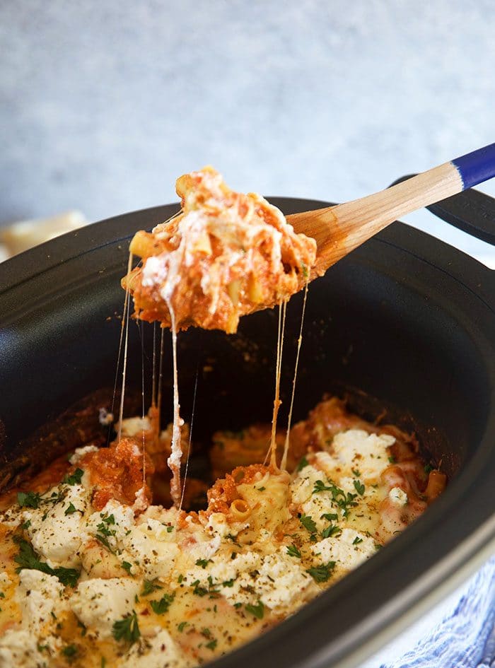 Slow Cooker Baked Ziti in a crock pot with a spoon full of ziti and melted cheese pulling into the pot.
