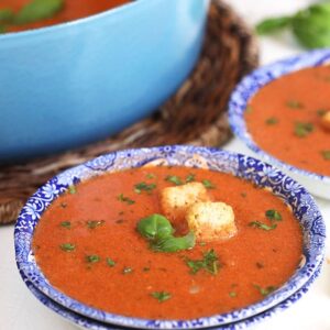 Tomato Basil Bisque in a blue and white bowl with croutons and basil on a white background.