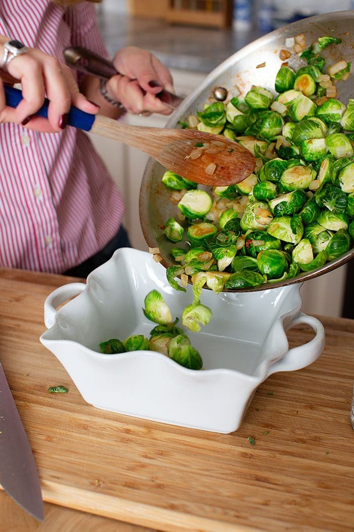 Sauteed brussel sprouts being poured into a baking dish.