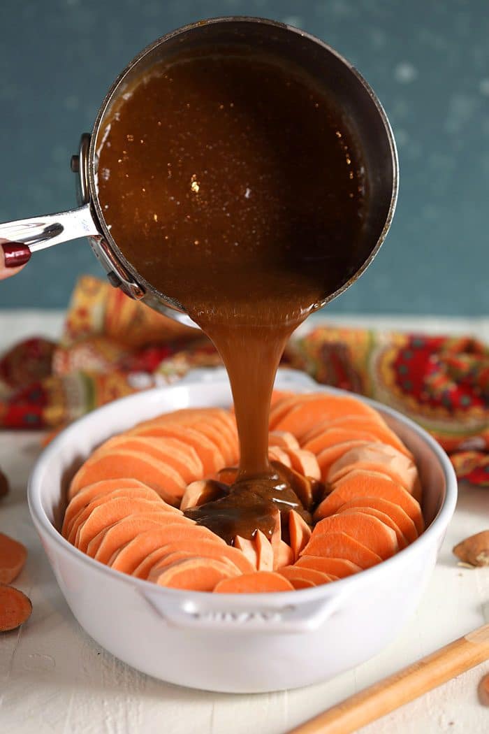 Yams in a baking dish with syrup being poured over them.