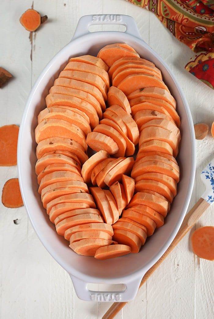 Yams sliced and arranged in a row in a white baking dish.
