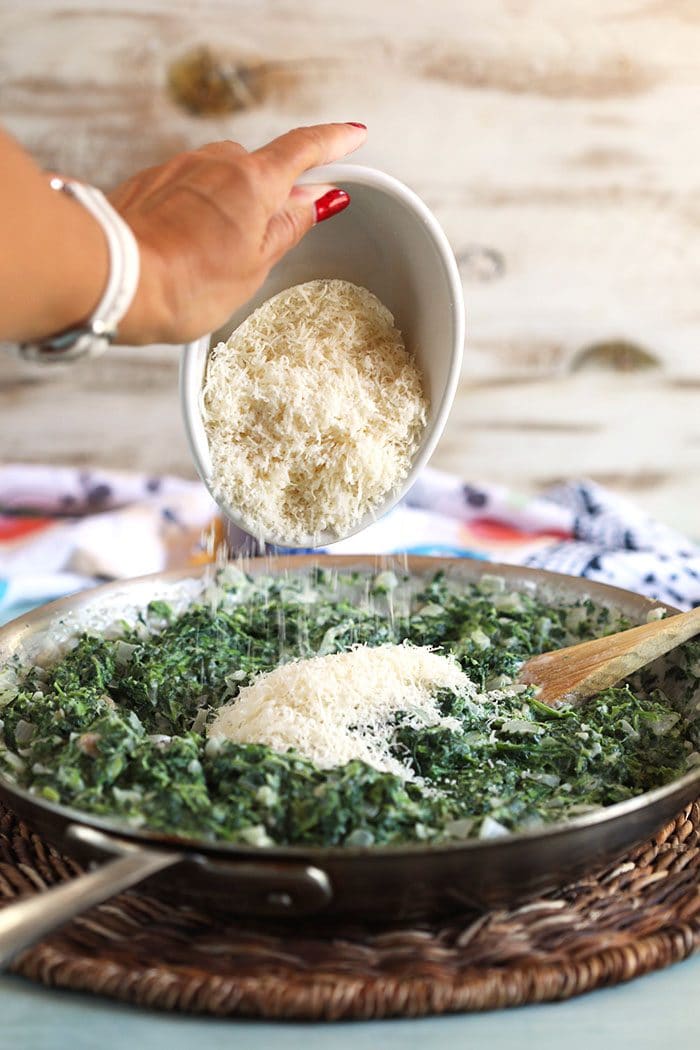 Cheese being poured into a skillet with creamed spinach.