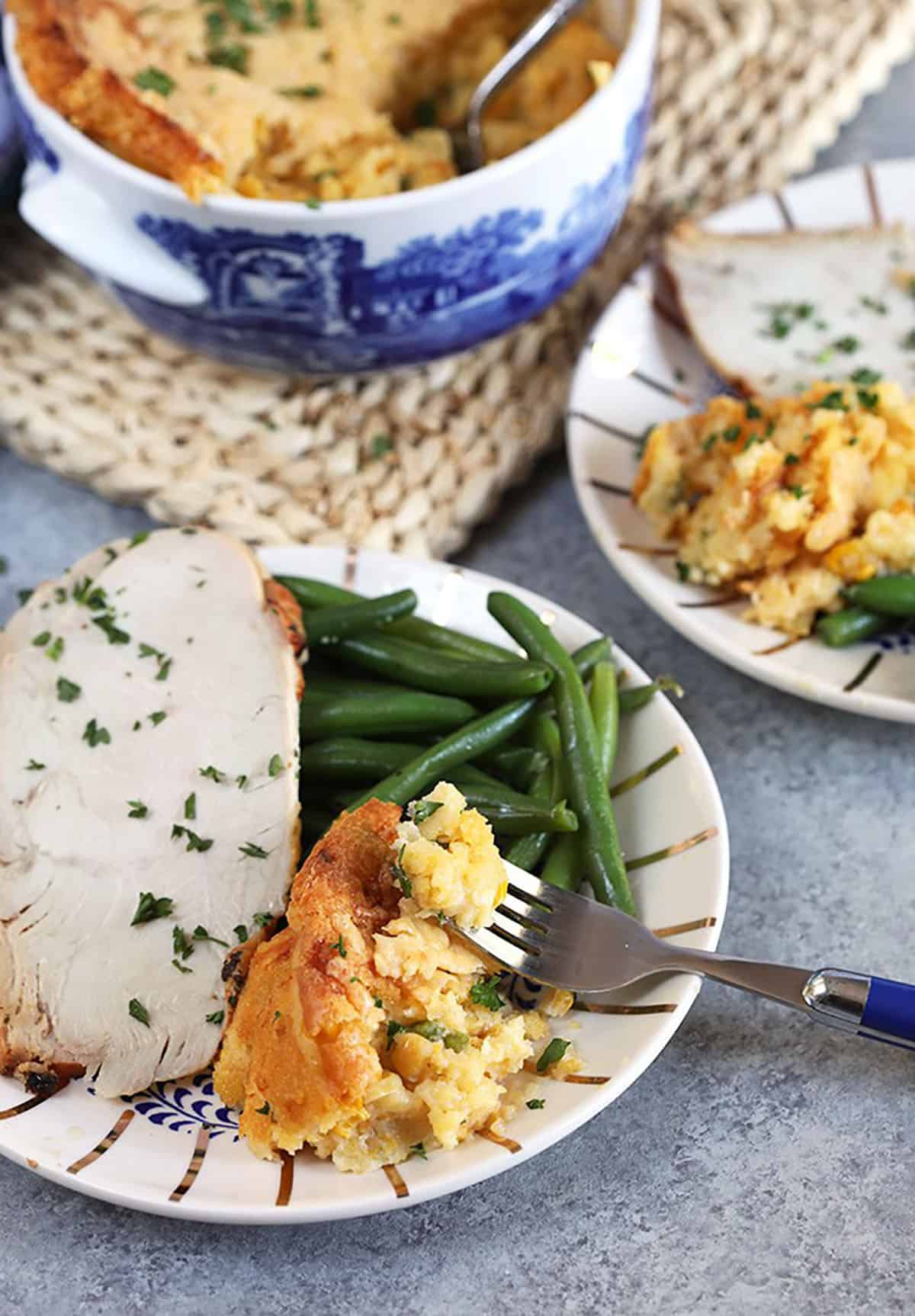 Cheesy Corn Casserole on a white plate with turkey and green beans.