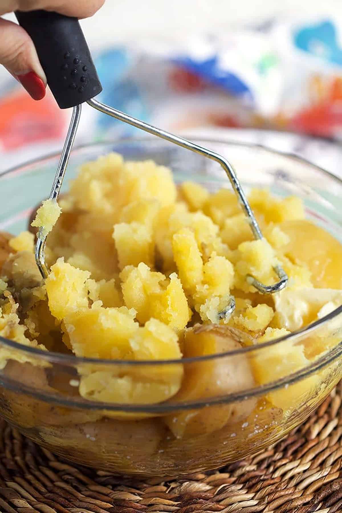 Potatoes being mashed with a potato masher in a glass bowl