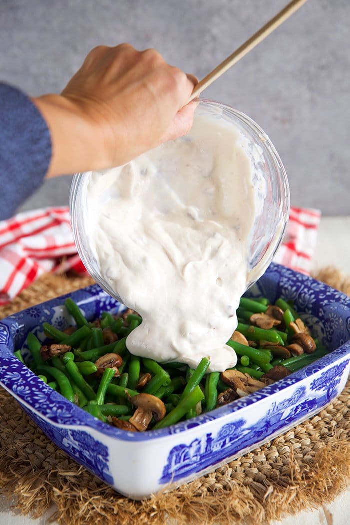 Green bean casserole with cream sauce being poured over top.