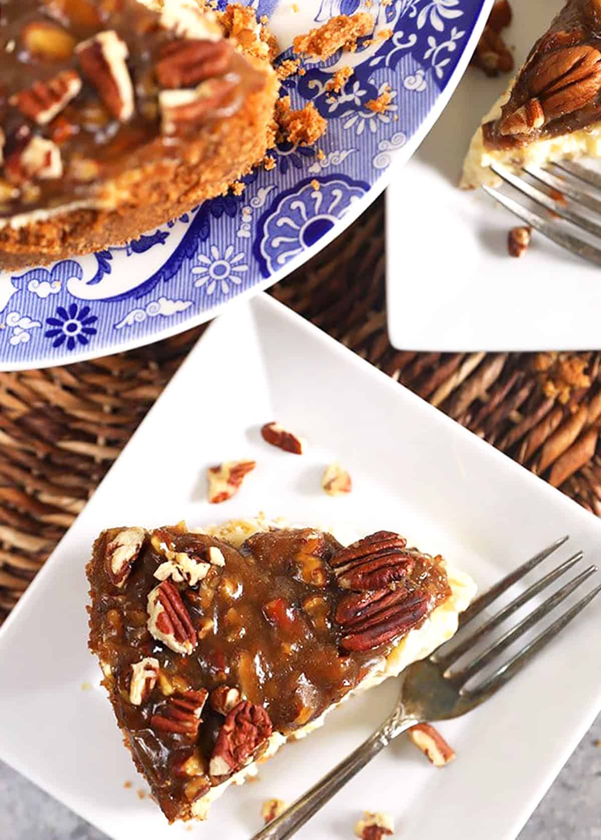 Slice of pecan pie cheesecake on a white square plate with a silver fork.