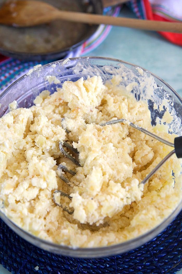 Potato pierogi filling in a bowl with a potato masher.