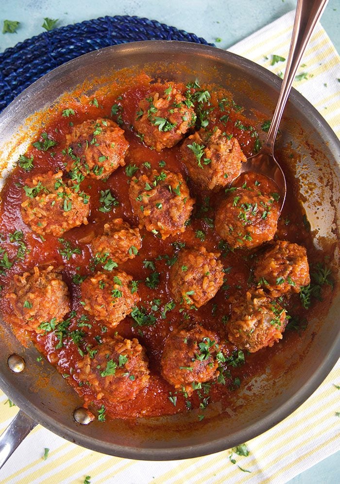 Overhead shot of porcupine meatballs in tomato sauce in a skillet with a spoon.
