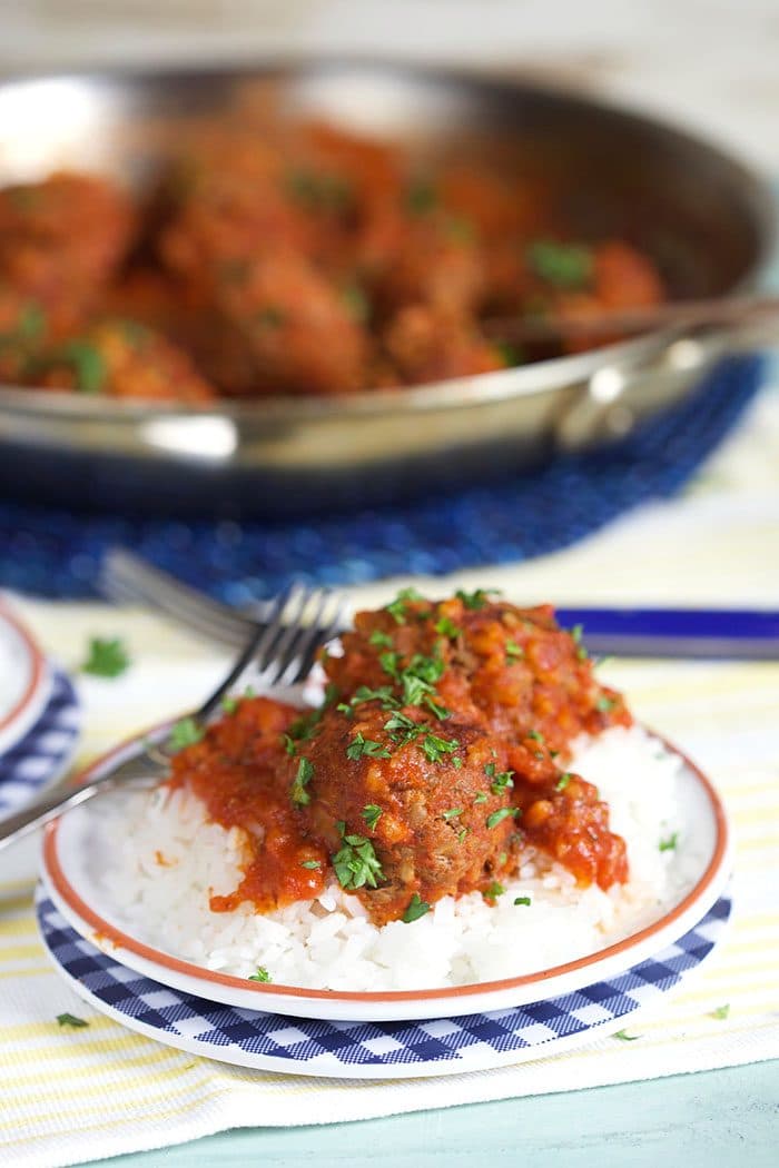 Easy Porcupine Meatballs in red sauce over a bed of rice with a skillet in the background.