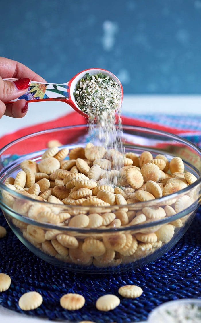 Ranch seasoning being poured over a bowl of oyster crackers.