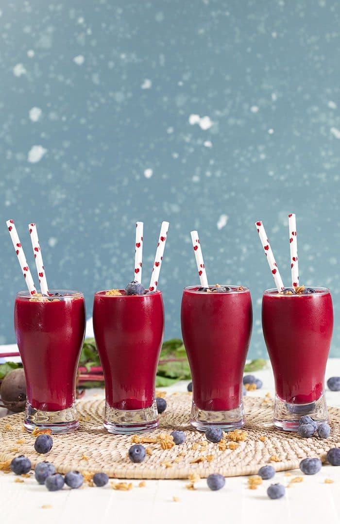 Four berry beet smoothies in a line on a blue background.