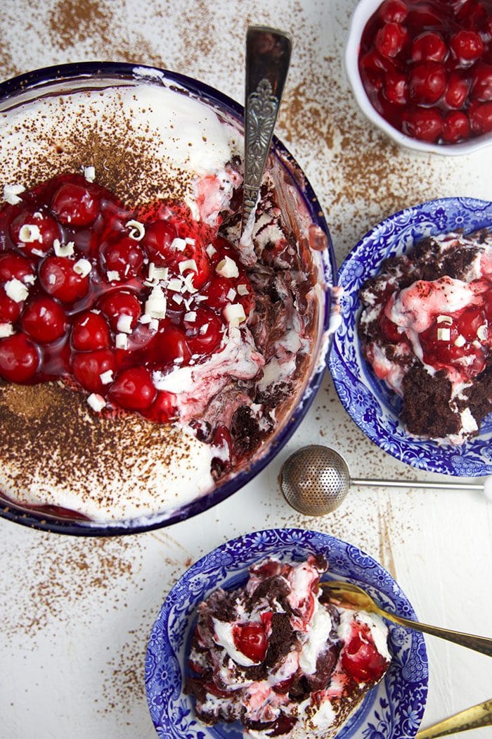 overhead shot of black forest brownie trifle with a scoop taken out and two bowls with servings of trifle in them.