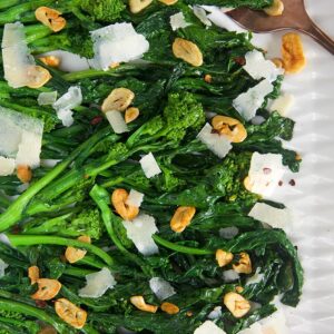 Overhead shot of broccoli rabe with garlic on a white platter.