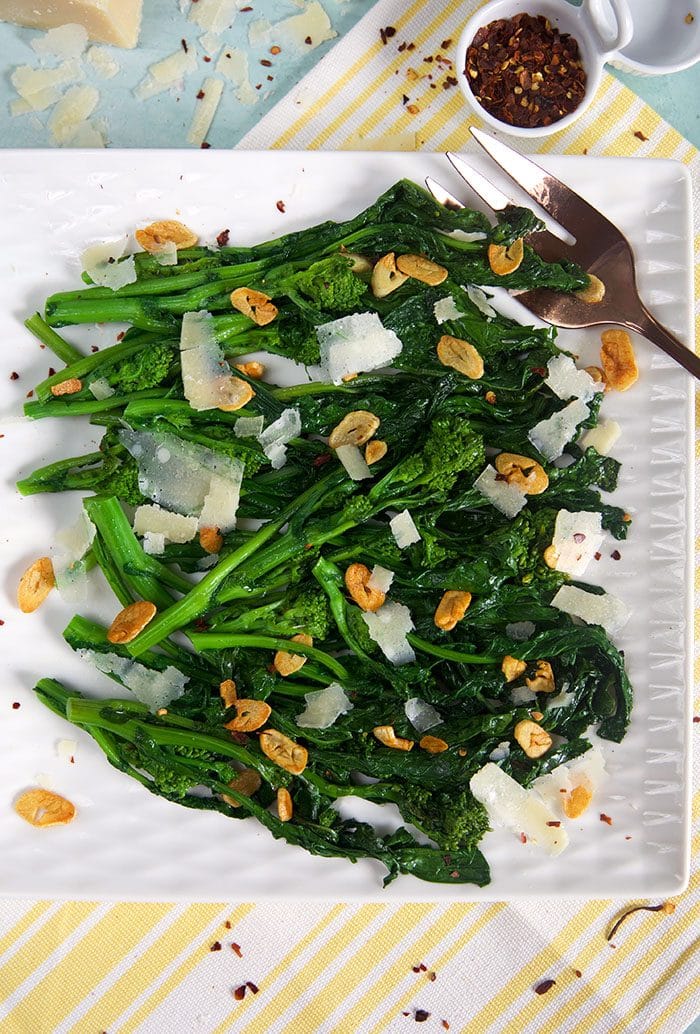 Broccoli rabe on a white square platter with crushed red pepper flakes in a bowl.