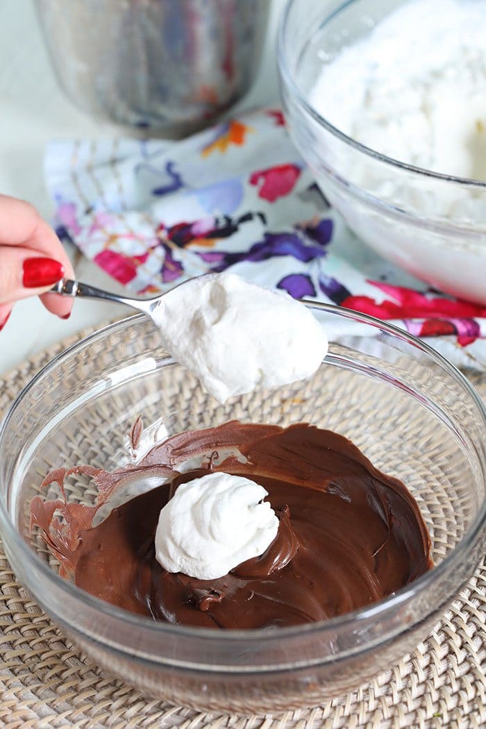 Melted chocolate in a glass bowl with whipped cream being added.