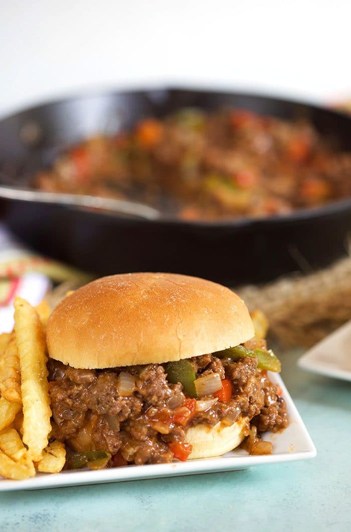 Philly cheesesteak sloppy joe on a white plate with a skillet in the background.