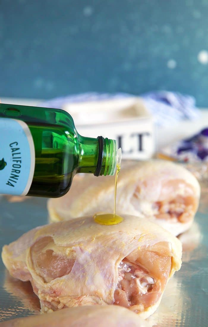 Olive oil being drizzled on a bone in skin on chicken breast.
