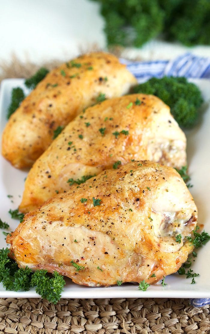 Golden crispy roasted chicken breasts on a white platter with parsley.