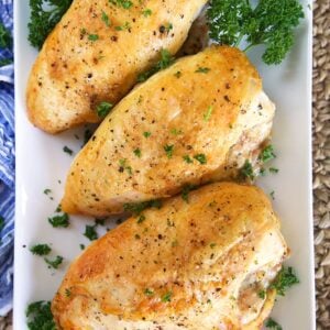 Three crispy roasted chicken breasts on a white rectangular platter.