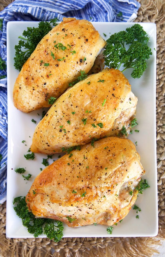Three crispy roasted chicken breasts on a white rectangular platter.