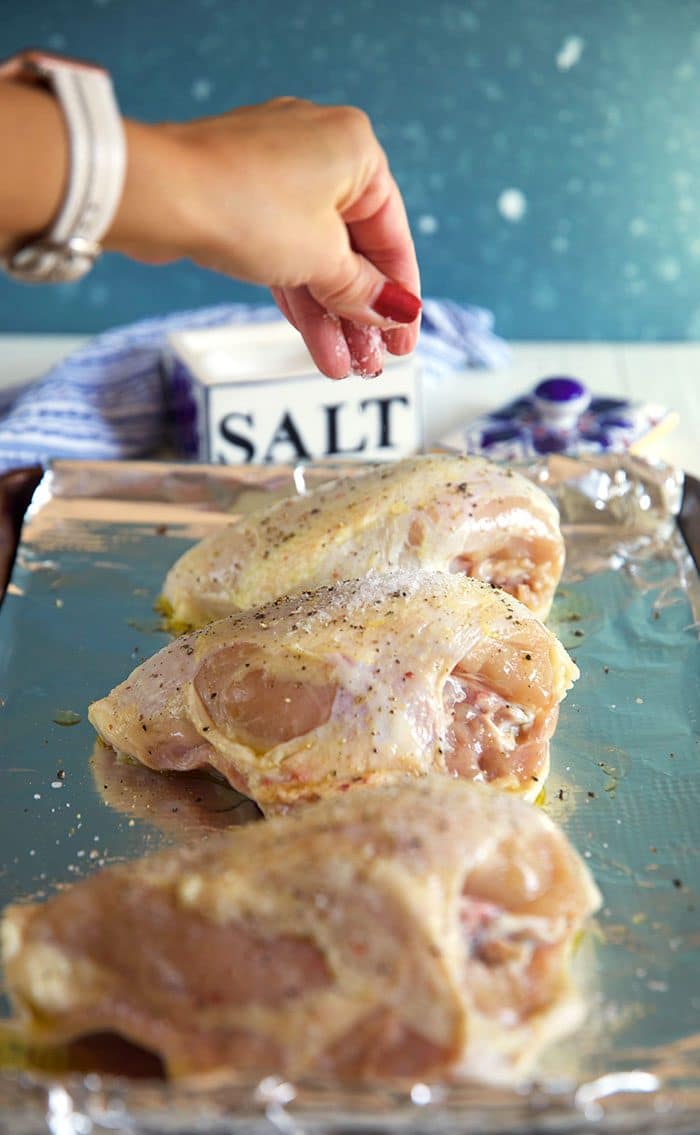 Salt being sprinkled on a bone in chicken breast.