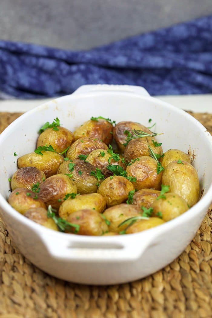 Roasted baby potatoes in a white baking dish with herbs sprinkled over them.