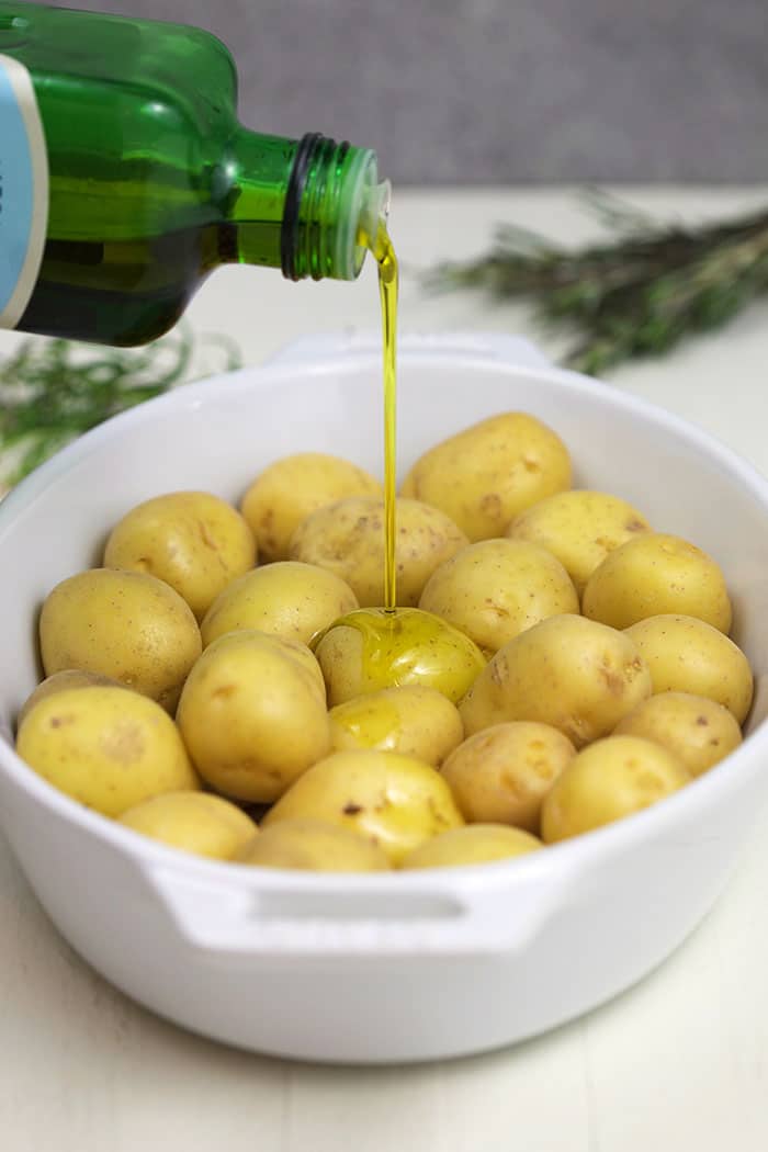 Olive oil being poured over the potatoes in a white casserole.