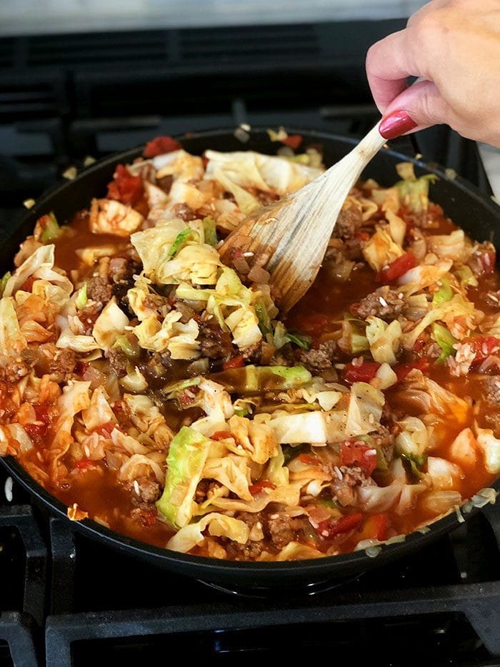 Stuffed cabbage casserole being stirred on a stovetop.
