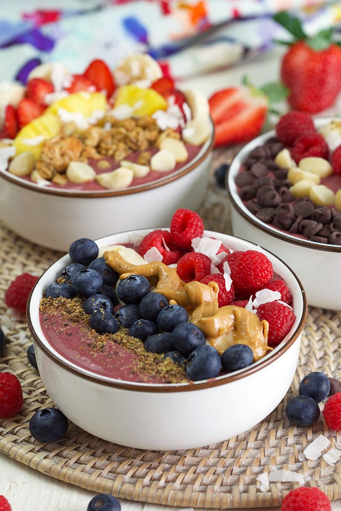 three acai bowls with fruit toppings.