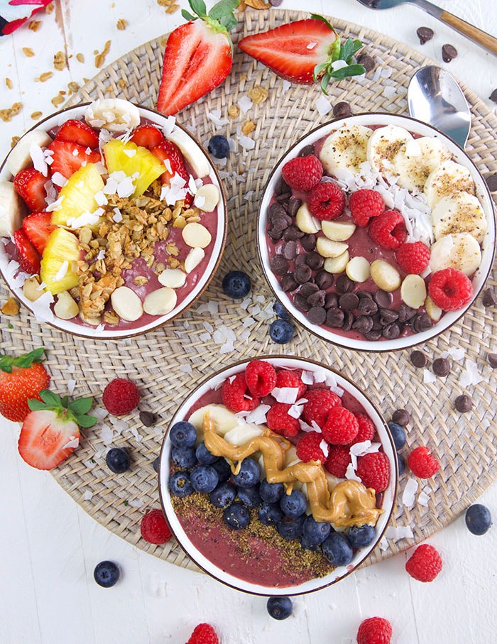 overhead shot of three acai bowls on a wicker placemat.
