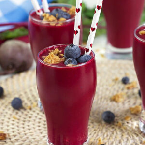 Berry Beet Smoothie in a small pilsner style glass with a paper straw with hearts on it.