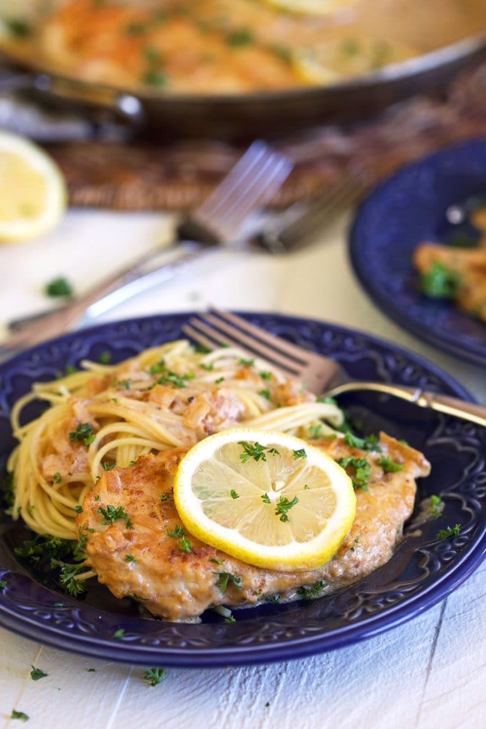 Chicken scallopini on a blue plate with pasta and a lemon slice.