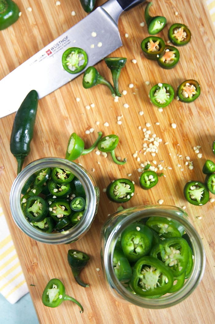 Overhead shot of sliced jalapeños on a bamboo board and in a jar.