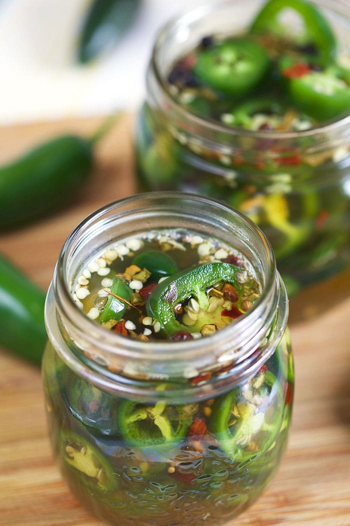 jalapeños in jars with pickle brine on a bamboo board.