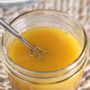 apple cider vinaigrette dressing in a glass jar with a whisk.