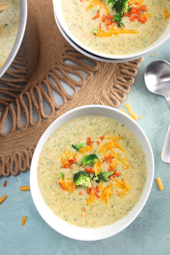 Broccoli Cheddar soup in a white bowl with a spoon on a blue background.