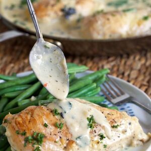 Chicken florentine on a plate with green beans and a spoon pouring sauce over the chicken.