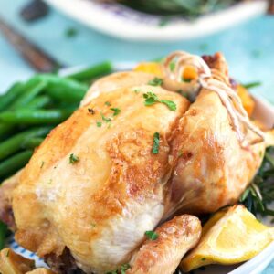 Close up of cornish hen on a white plate with a lemon wedge and green beans.