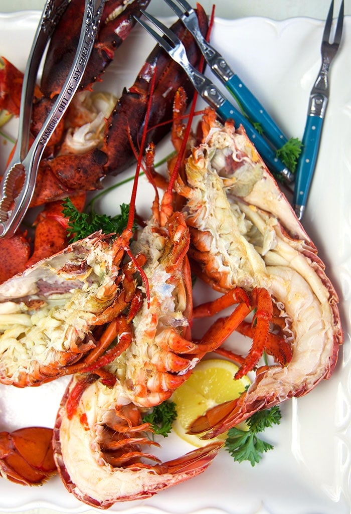 Cooked whole lobster cut in half on a white platter.