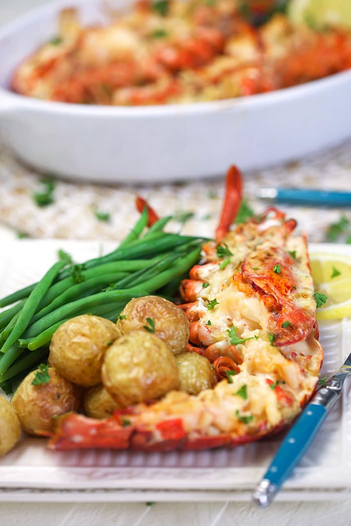 Lobster thermidor on a plate with potatoes and green beans.